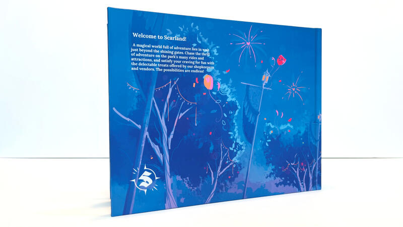 The Scarland Artbook on a white surface with a white background. It is stood such that the back of the book is visible. The text reads: "Welcome to Scarland! A magical world full of adventure lies in wait just beyond the shining gates. Chase the thrill of